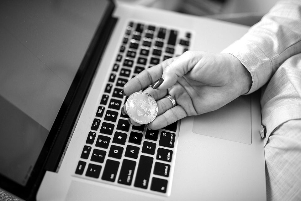 Close-up of a Bitcoin physical coin in a womans hand and a laptop on her lap