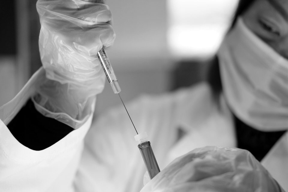 Japanese female scientist wearing plastic gloves holding syringe and vial, researching a coronavirus vaccine